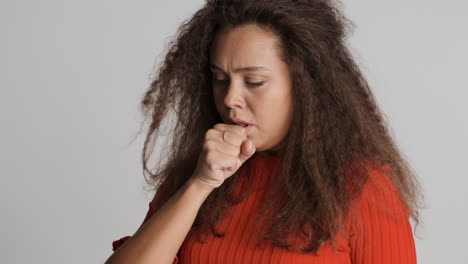 caucasian curly haired woman coughing in front of the camera.