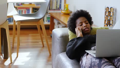 Woman-talking-on-mobile-phone-while-using-laptop-on-sofa-at-home-4k