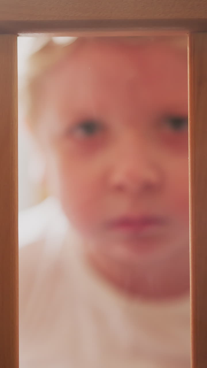 Upset blond toddler looks out of cot grabbing wooden planks with hands. Scared little boy looks ahead sitting in nursery alone closeup slow motion