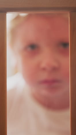 upset blond toddler looks out of cot grabbing wooden planks with hands. scared little boy looks ahead sitting in nursery alone closeup slow motion