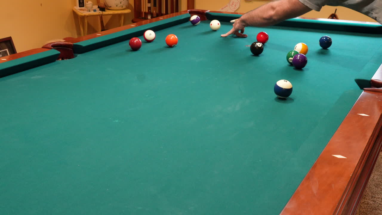 Man Playing 8 Ball Pool Shoots Several Striped Balls into Pockets on a Brunswick Table for Billiards with Green Felt in Basement of Home, Open Bridge Hand and Wooden Cue Stick, Wide Angle No Faces