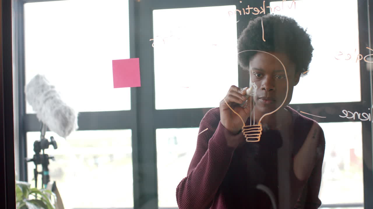 African american casual businessman drawing on glass wall at home office, copy space, slow motion
