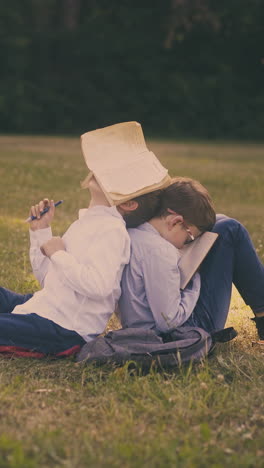 cute boys have fun with textbooks preparing for hard exams sitting on fresh lawn in green park after lessons