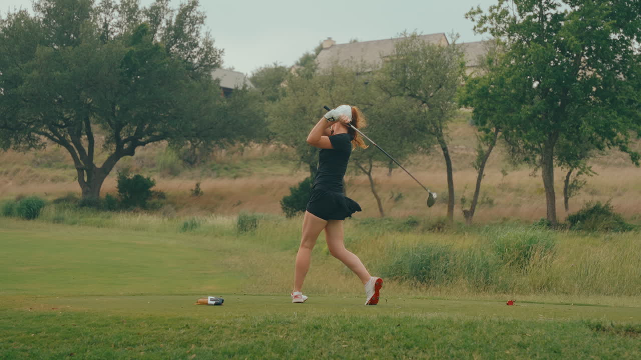 Slow-motion shot of a female golfer from behind, crushing a powerful drive off the ladies tees. The wind blows her skirt as she swings, showcasing strength and grace on a lush outdoor golf course.