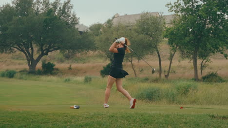 slow-motion shot of a female golfer from behind, crushing a powerful drive off the ladies tees. the wind blows her skirt as she swings, showcasing strength and grace on a lush outdoor golf course.