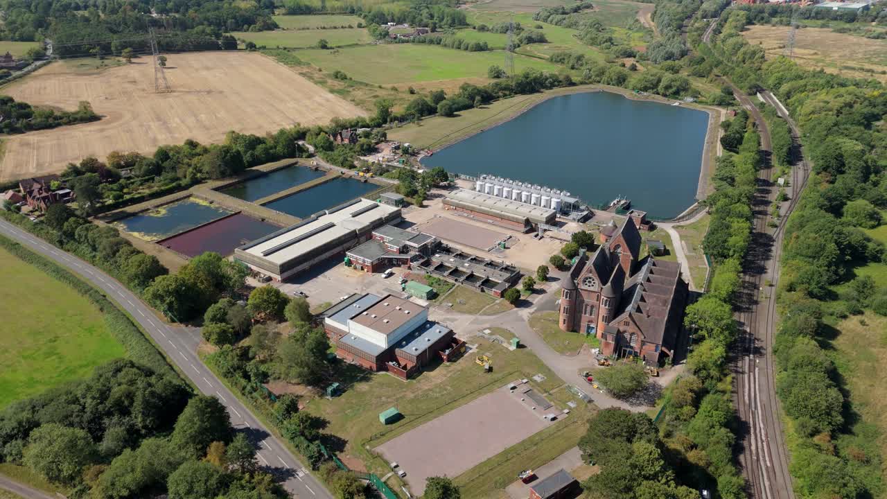Aerial drone video of wastewater sewage treatment plant with water silos and infrastructure in Birmingham, England, UK, surrounded by rolling green landscape