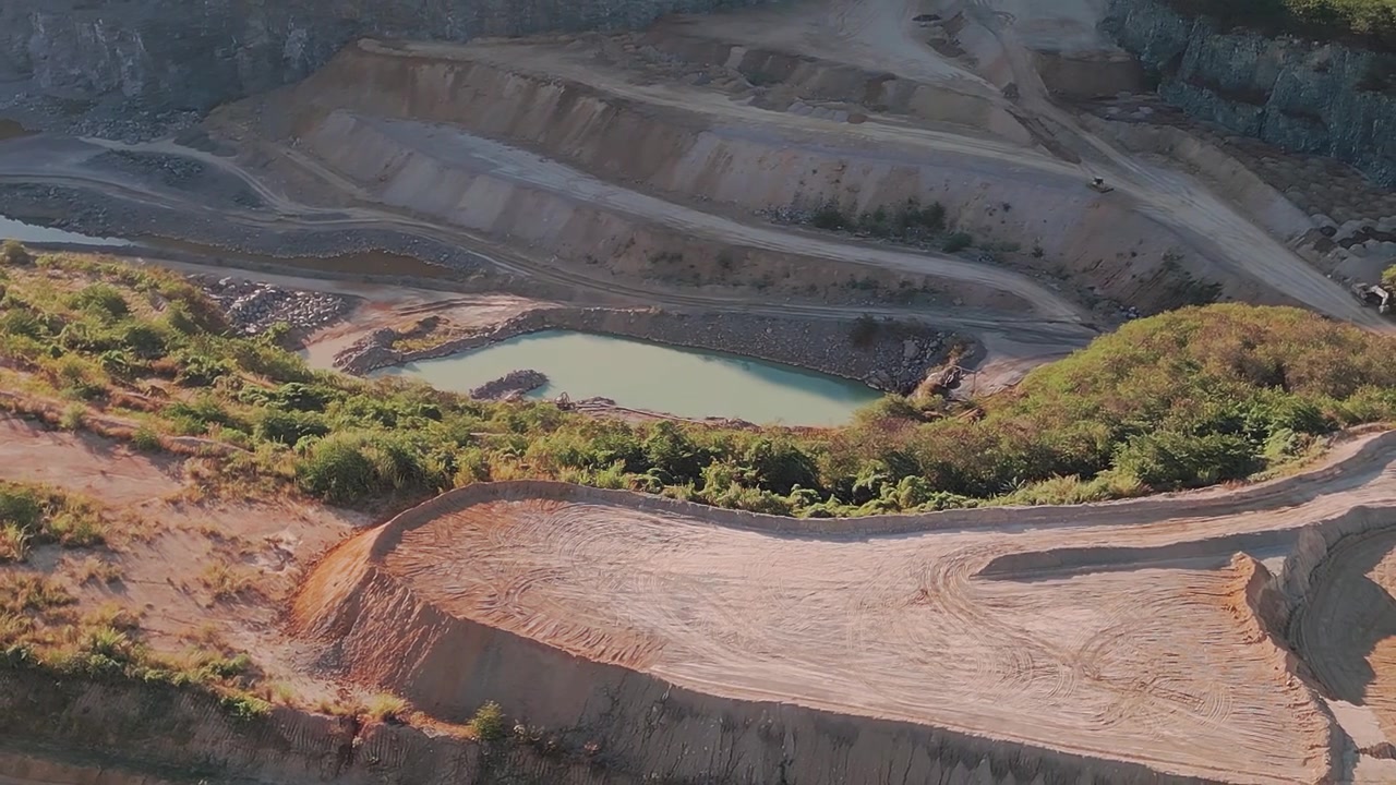 Limestone extraction quarry in Fercal, Brasilia, showing terraced earthworks, a turquoise tailings pond, and the surrounding native Cerrado biome, drone orbit establishing shot.