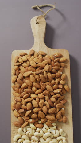 video vertical de nueces de almendra y caju apiladas en una tabla de cortar de madera con fondo de lila