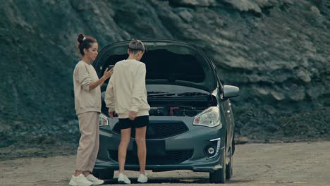 two people facing car trouble with a broken down vehicle in a desolate, rocky area