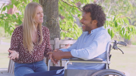 smiling mature couple with man sitting in wheelchair talking in park together