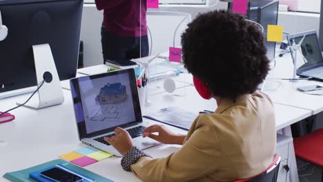 mixed race businesswoman wearing face mask sitting using a laptop in modern office