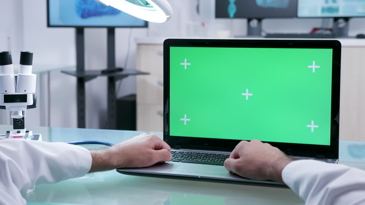 Scientist working on laptop with green screen in a lab