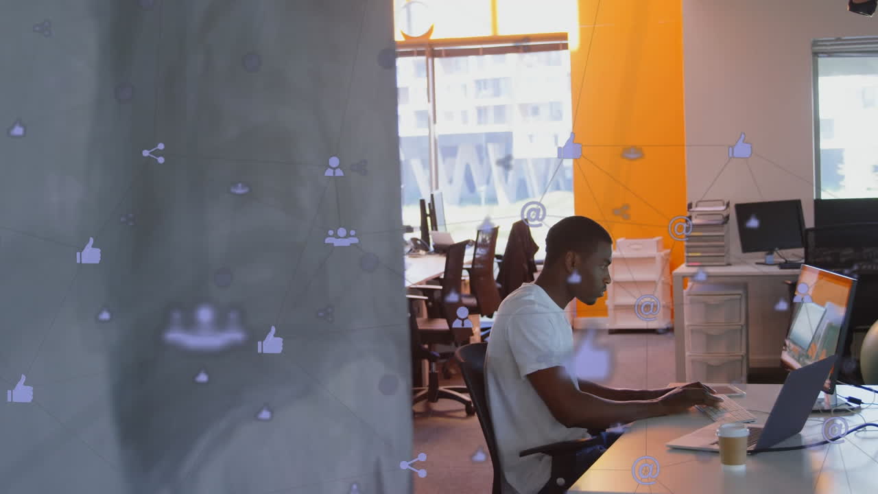 Animation of network of digital icons against african american man using computer at office