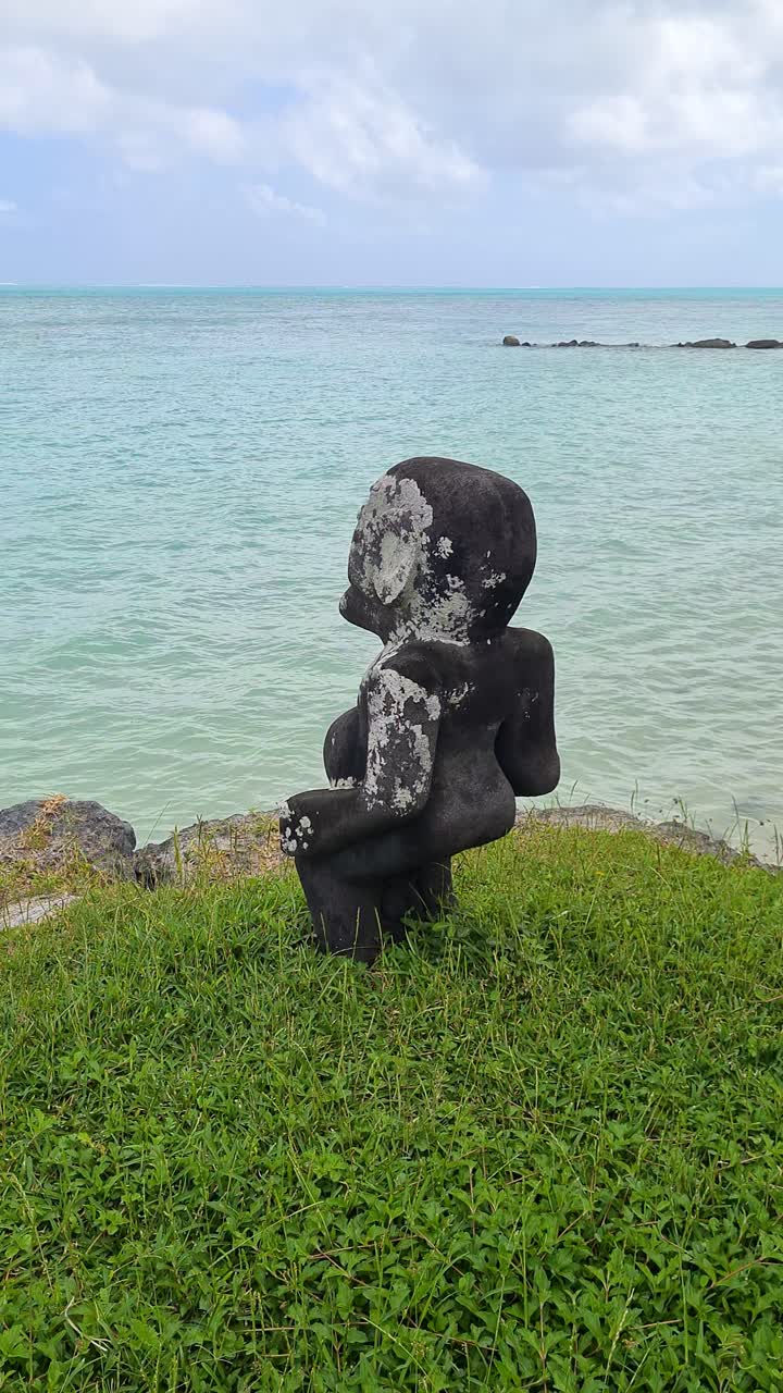 Statua antica in pietra su costa erbosa vicino al mare turchese