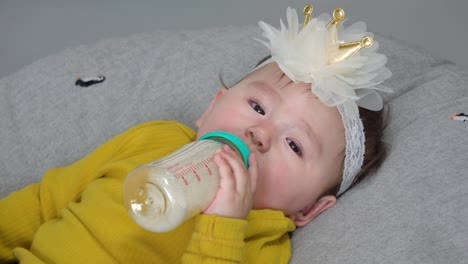 pretty 11 month baby girl drinks formula milk from bottle lying on donut cushion