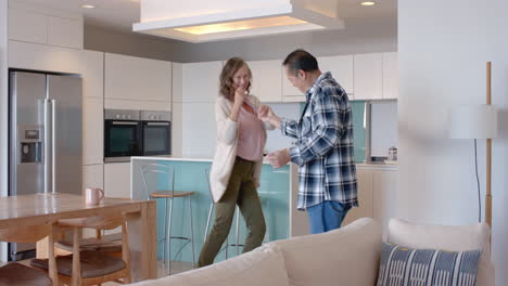dancing together, senior couple enjoying time in modern kitchen at home
