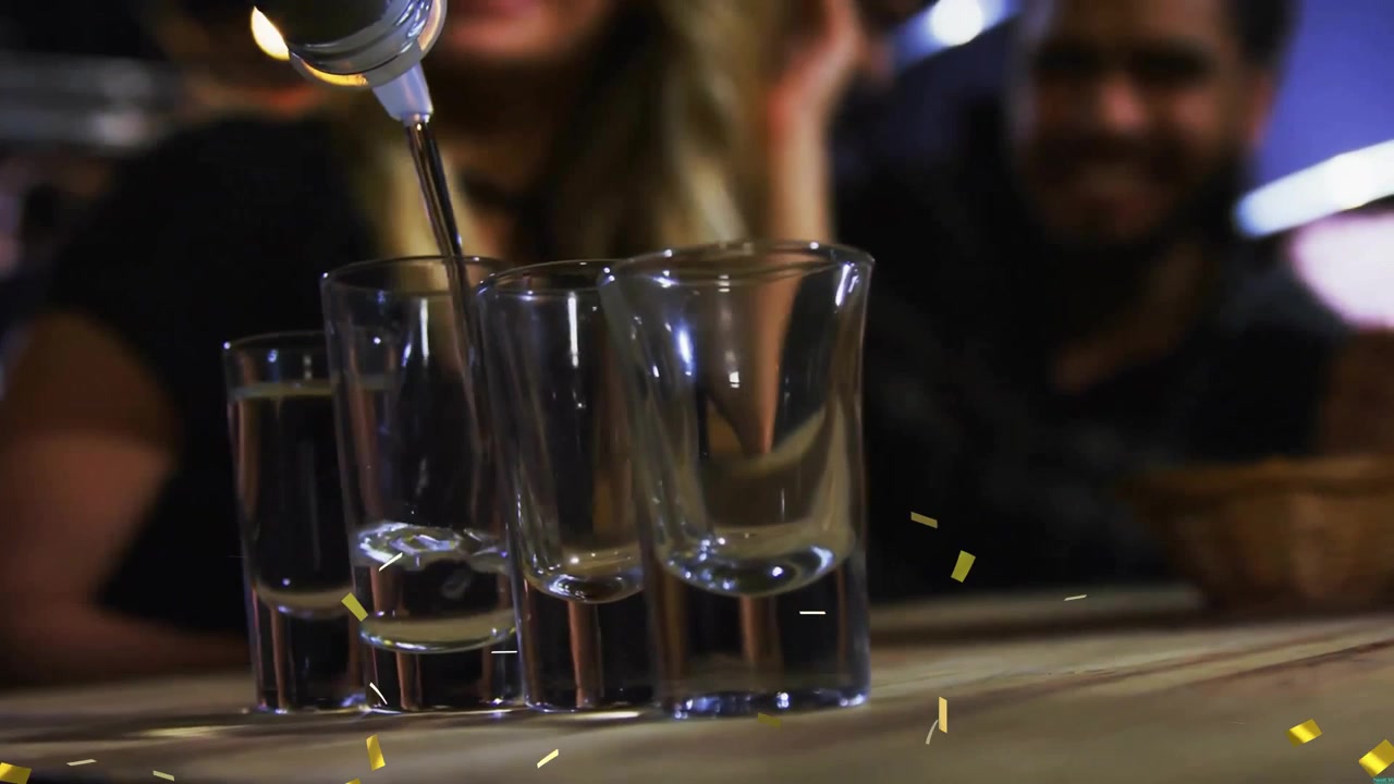 Barkeeper gießt Spirituosen in Schnapsgläser an der Bar, während ein Paar inmitten fallenden Konfettis feiert.