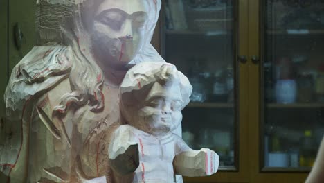 craftsman checks details of Madonna and Child sculpture, revealing focused craftsmanship and detailed woodworking tools create an artistic atmosphere