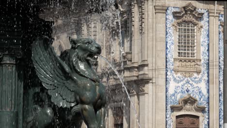 closeup of winged lion statue fountain spraying water in front of historic baroque church facade with blue azulejos in viseu, portugal. bright daylight highlights stone and ceramic details