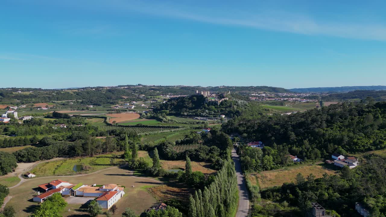 A distant aerial view captures the impressive Castle of Óbidos, Portugal, a medieval fortress surrounded by picturesque landscapes, showcasing its historic architecture and strategic hilltop position.