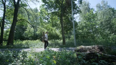 young man walking with guitar on street near forest