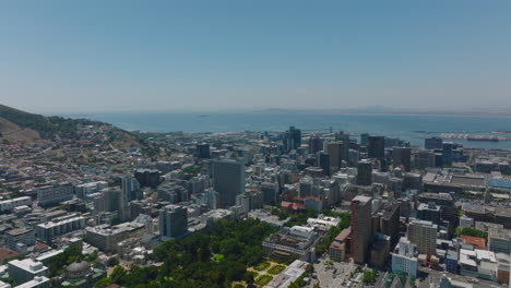 Aerial-descending-footage-of-multistorey-office-or-apartment-buildings-in-urban-borough.-Sea-surface-in-background.-Cape-Town,-South-Africa