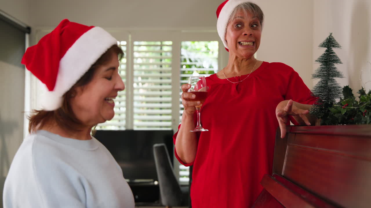 At Christmas, Senior women wearing Santa hats laughing and enjoying holiday drinks at home