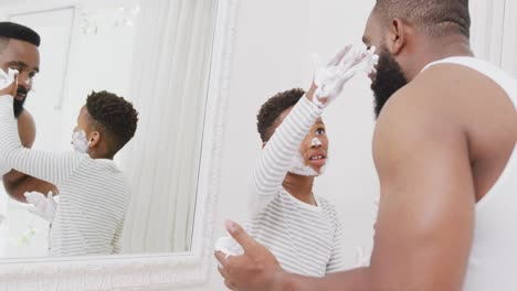 happy african american father and son applying shaving cream on face in bathroom, in slow motion