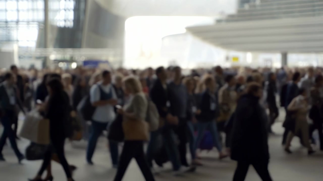 Scena interna sfocata di un moderno atrio di transito con una persona in silhouette che porta uno zaino leggermente a sinistra del centro. Il piano intermedio affollato mostra pendolari.
