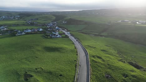 countryside road winding through green fields near a coastal village at dusk