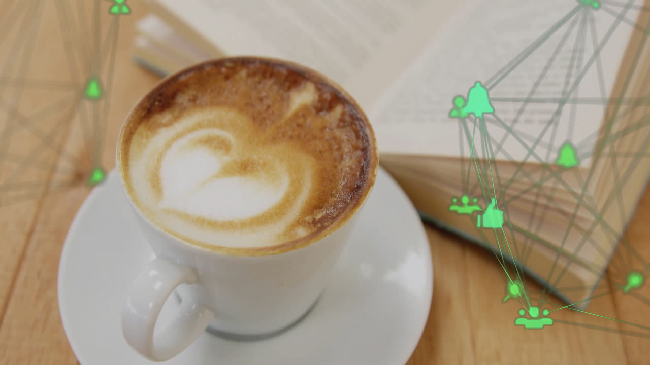 White coffee cup displaying heart latte art on table while green network icons floating above book