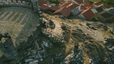 a girl walks down the stairs of the stone path at folgosinho castle as a group of tourists walk up and the drone flies over them