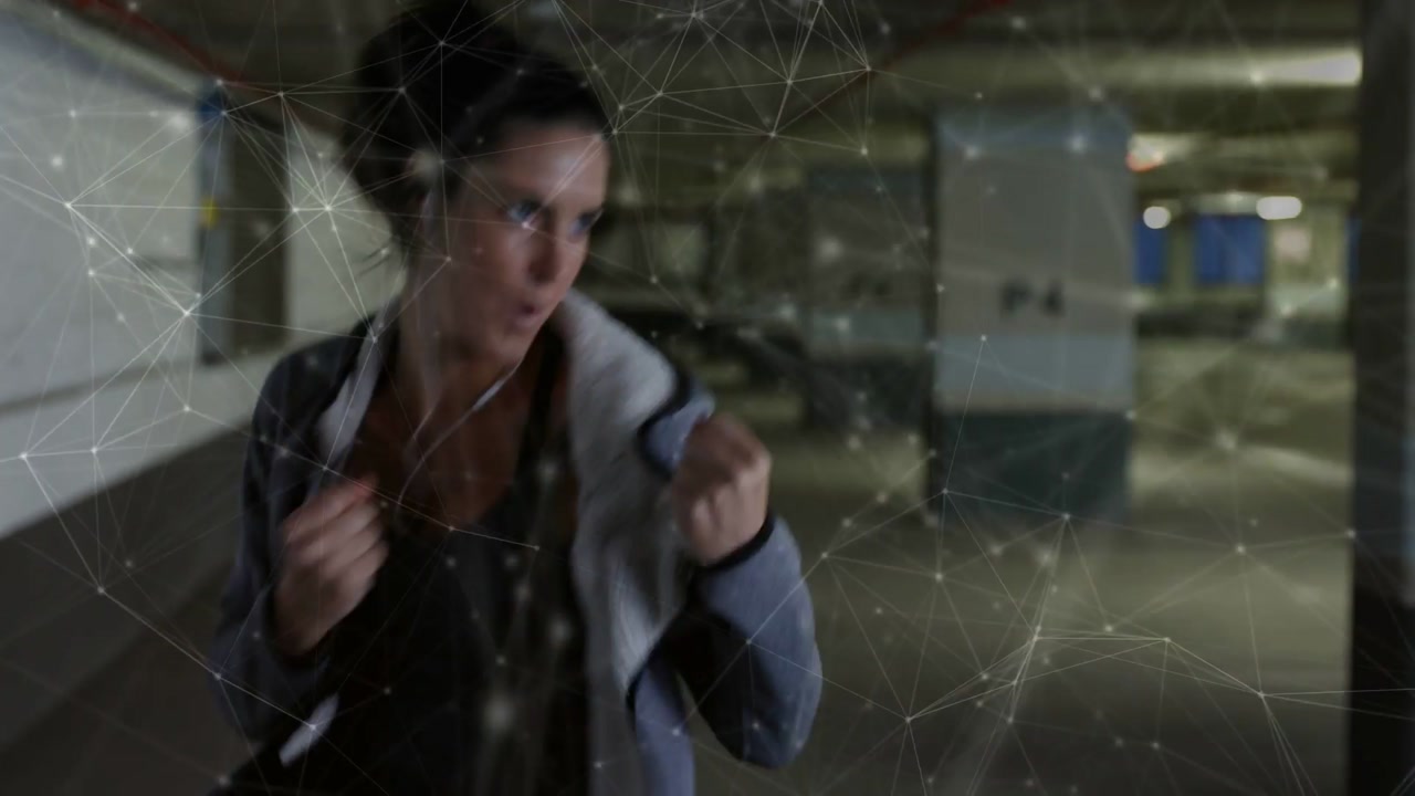 Woman rising from crouch with hoodie and training shadowboxing in garage, overlay crossing subject