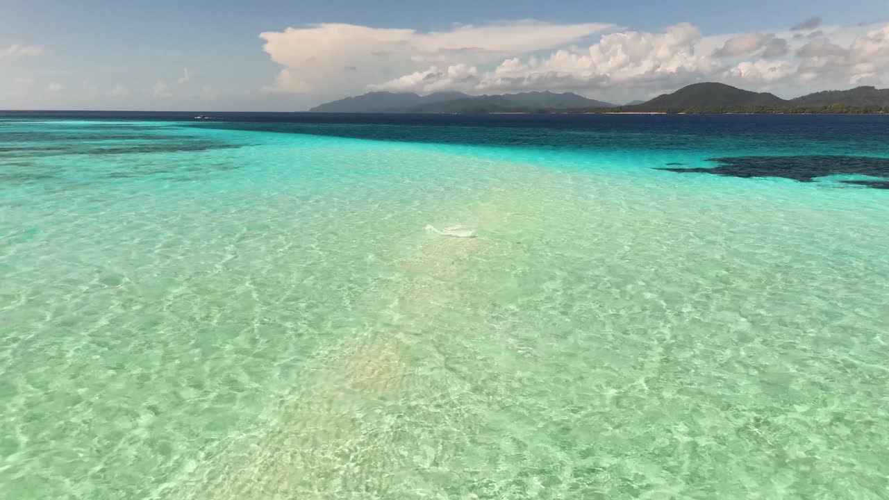 Pristine shallow turquoise waters stretch across the Candaraman Sand Bar in Balabac, Palawan, Philippines, revealing a stunning blend of colors, coral patches, and distant mountainous islands