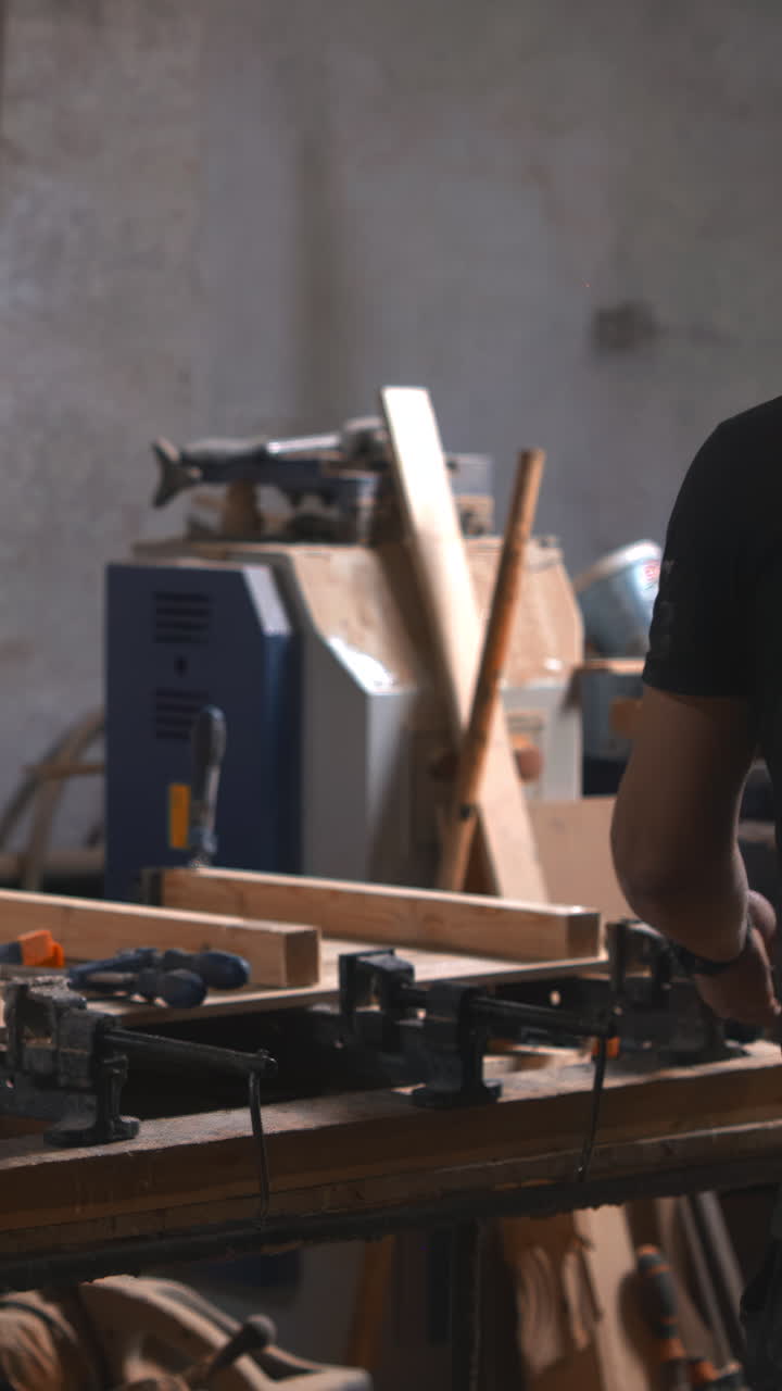 Carpenter Measuring Reclaimed Plank On Dim Workbench, Clamps And Hand Tools Scattered, Careful Planing. Media