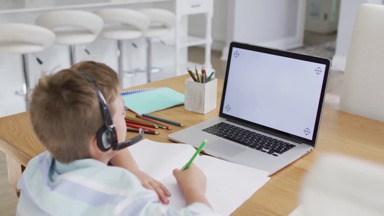 niño caucásico feliz durante la lección escolar en línea usando auriculares y computadora portátil, copie el espacio en la pantalla