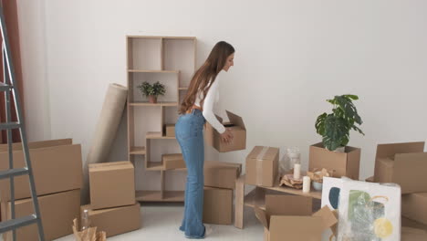 happy woman holding boxes and walking in empty apartment while smiling at camera