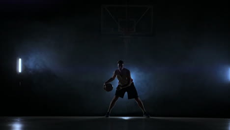 Skill-dribbling-basketball-player-in-the-dark-on-the-basketball-court-with-backlit-back-in-the-smoke.-Slow-motion-streetball