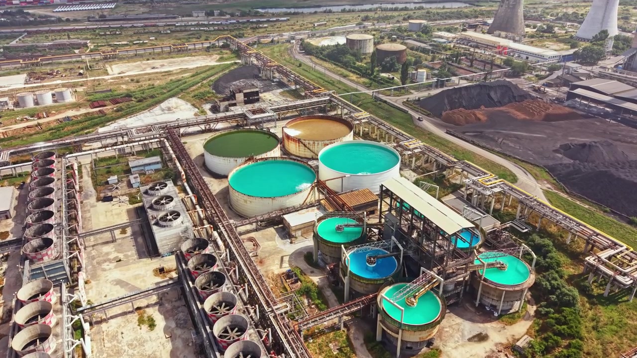 Industrial facility with large tanks and pipelines located near a power plant and storage area on a sunny day in an urban area