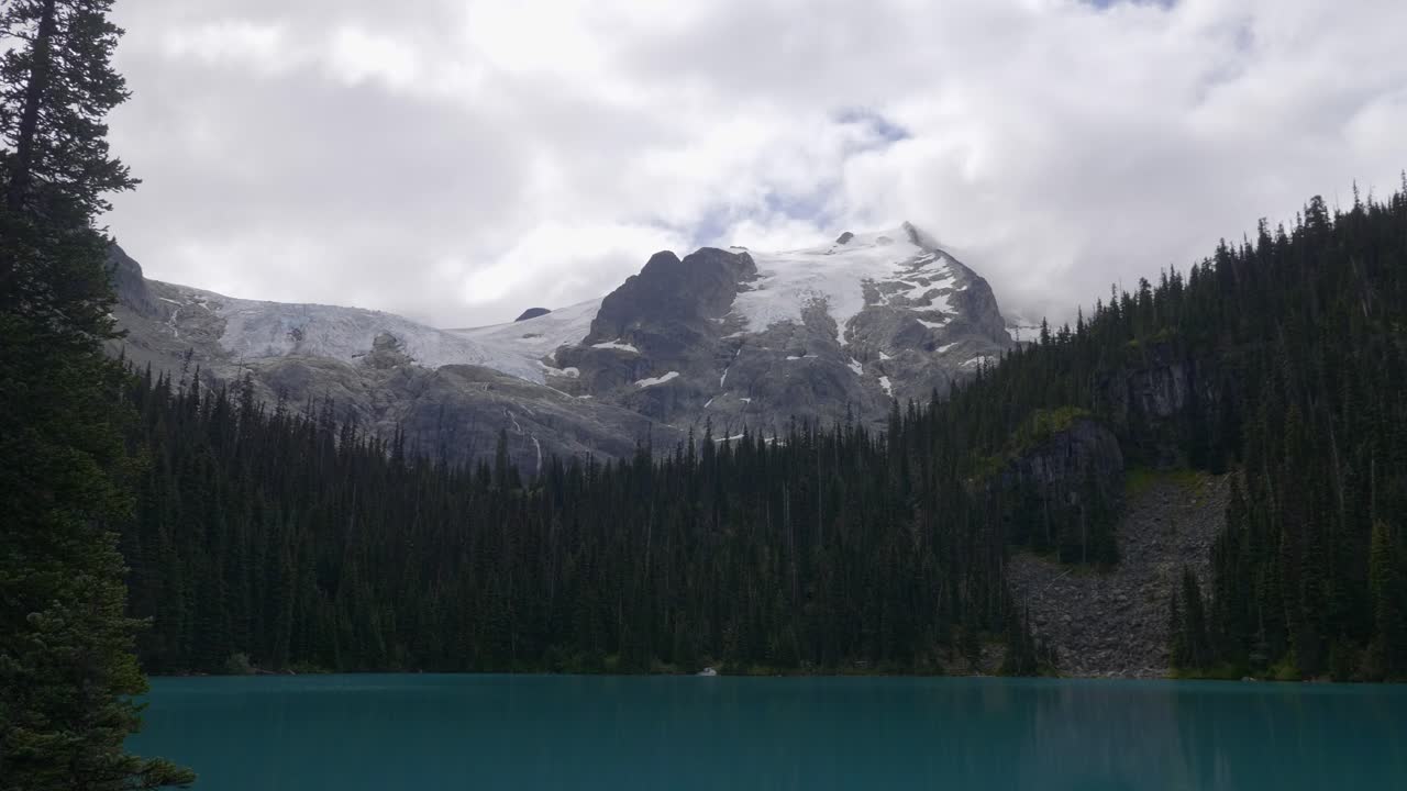 joffre lakes, pemberton, columbia británica, canadá - una vista de un sereno lago azul abrazado por una exuberante vegetación, con una montaña cubierta de nieve en el fondo - toma amplia