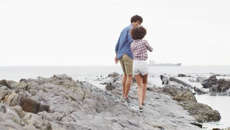 pareja afroamericana cogida de las manos caminando por las rocas cerca del mar