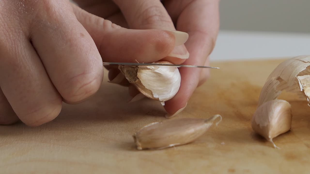 Person peeling garlic on wooden cutting board in the kitchen, close up
