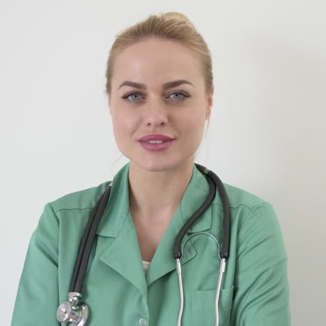 smiling female doctor in green medical coat with arms crossed posing looking at camera against white