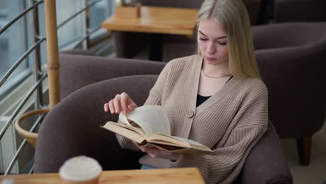 woman seated comfortably, relaxed as she reads her book, absorbed in her reading session, in a cozy study space with a warm coffee cup placed on the table