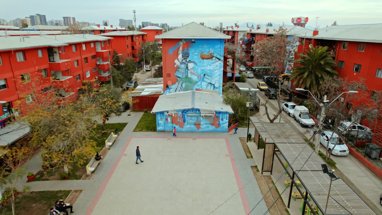 Static drone shot of children playing soccer with an adult in front of a mural at the San Miguel open air museum in Santiago, Chile.