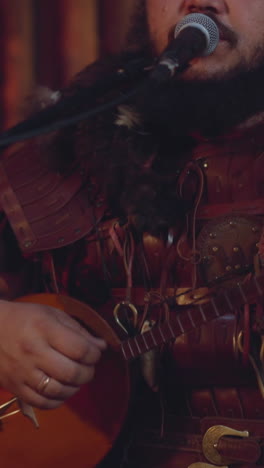 asian musician in leather clothes plays banjo and sings ancient song in ail room slow motion. folk music performer at ethnic concert. altai rhythms