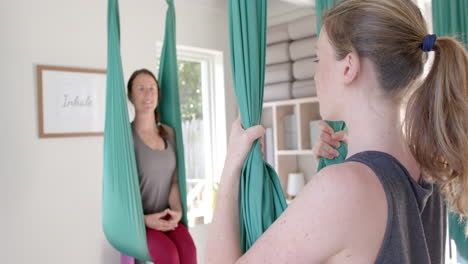 diverse fitness women exercising in aerial yoga class in big white room, slow motion