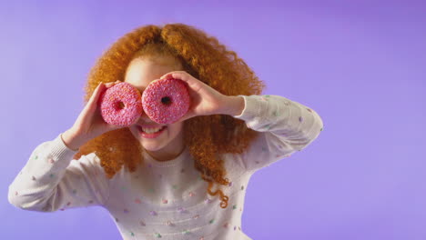 retrato de estudio de una niña con dos rosquillas frente a los ojos contra un fondo púrpura