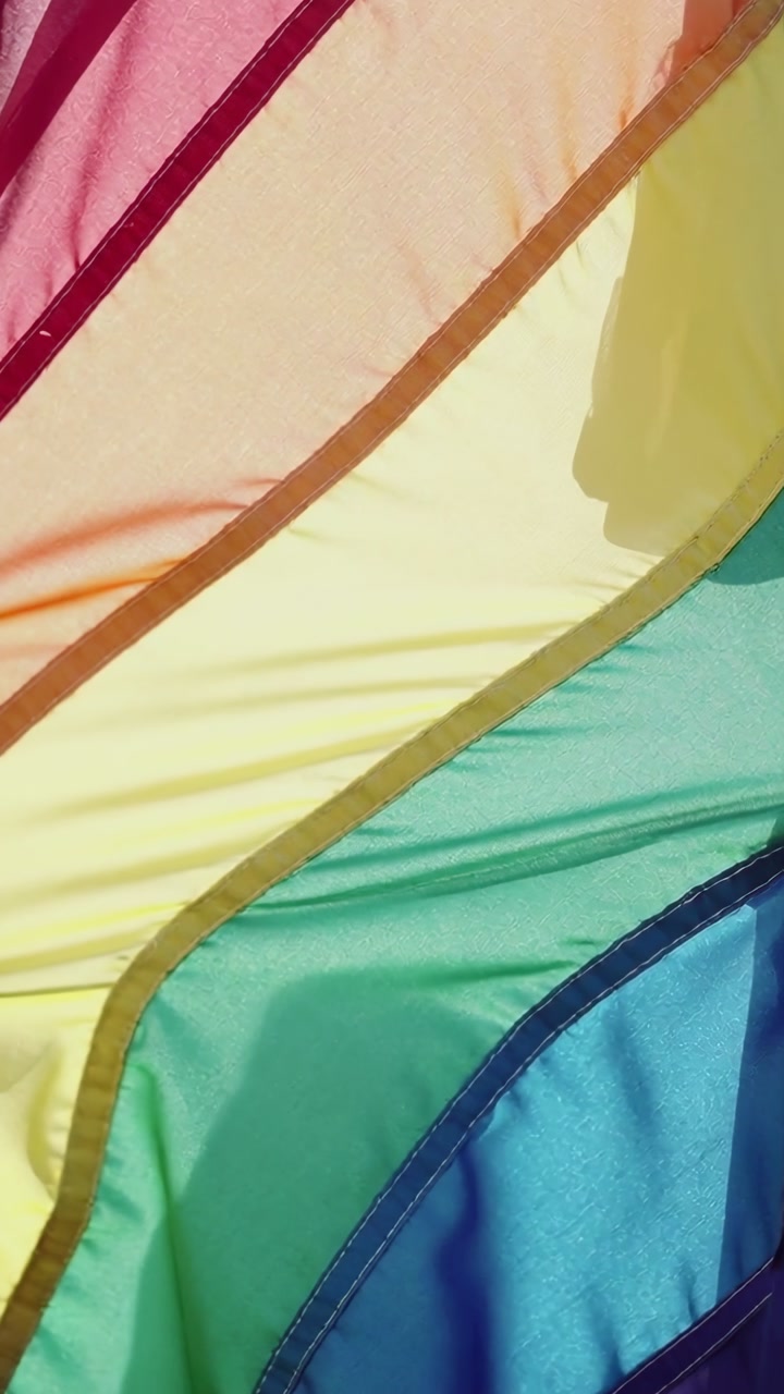 Vertical video: Entering hands gripping rainbow flag outside, purple sleeve tugging fabric rippling