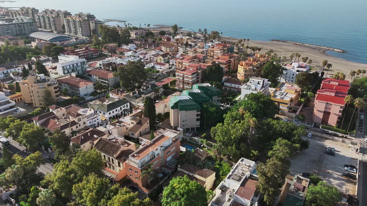Aerial view of Málaga, Spain, showing coastal buildings, beach, and birds flying across the scene